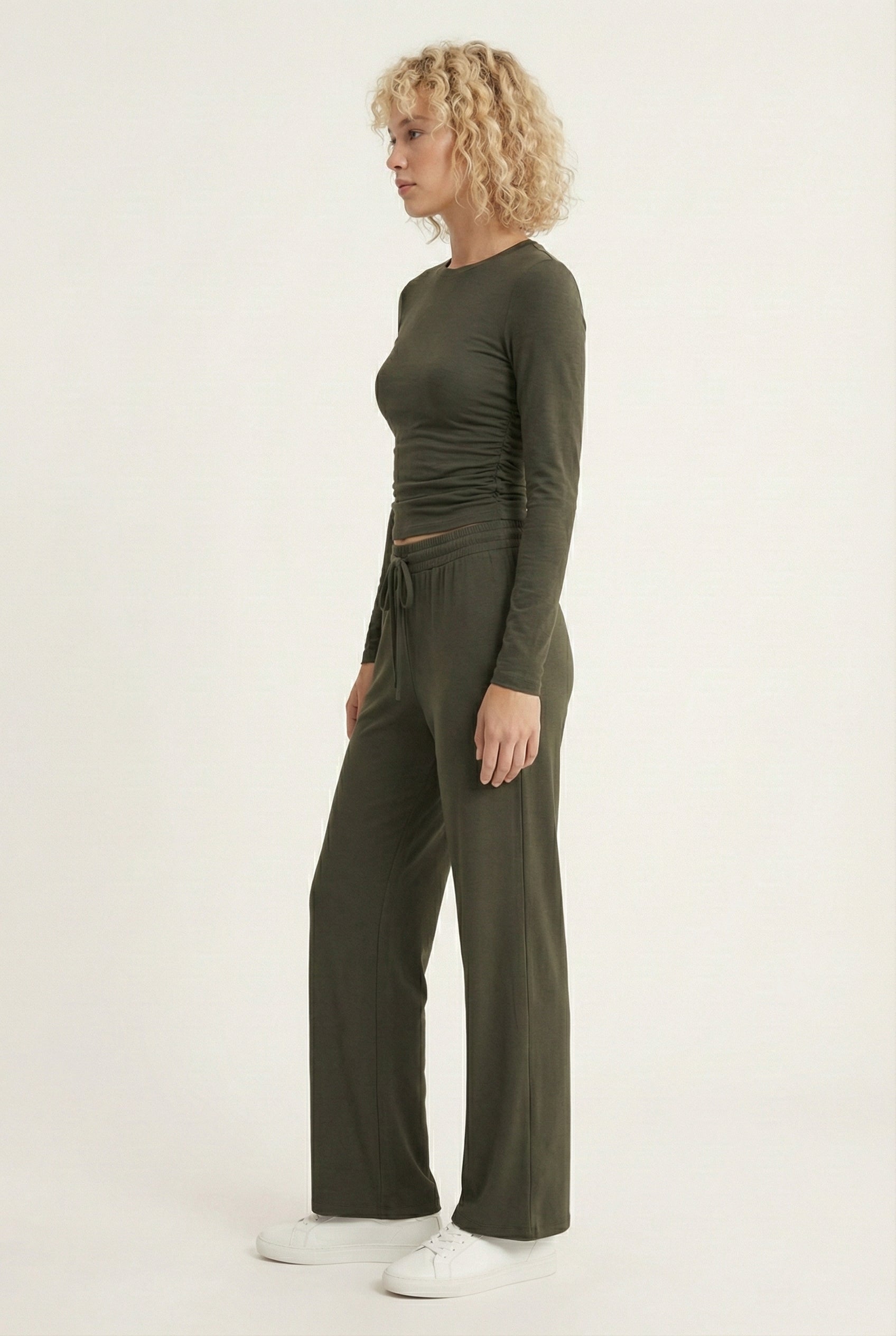 Model wearing The Rive Set sleek stretch lounge set in Cypress by Lohnr, featuring a ruched long-sleeve top and wide-leg drawstring pants