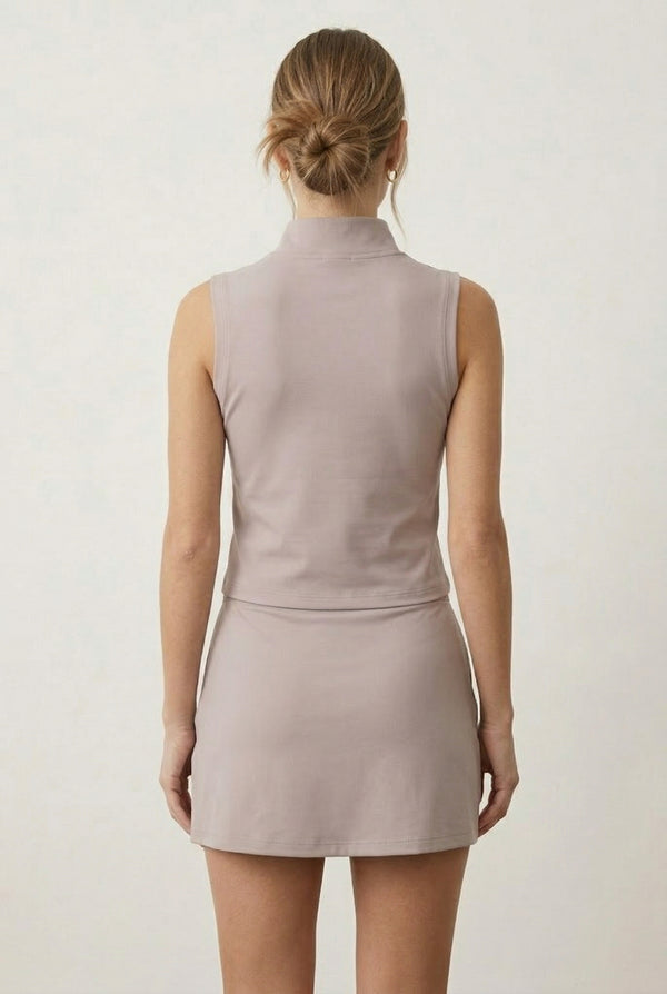 A woman posing in a Stone Veil colored sleeveless sporty dress featuring a zip-up mock neck.