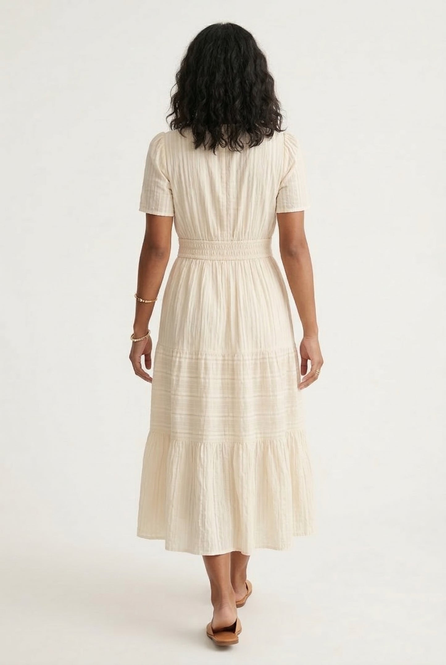 A woman posing in an Oat beige short-sleeve midi dress featuring a button-down bodice and flowy skirt.