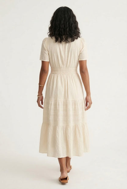 A woman posing in an Oat beige short-sleeve midi dress featuring a button-down bodice and flowy skirt.