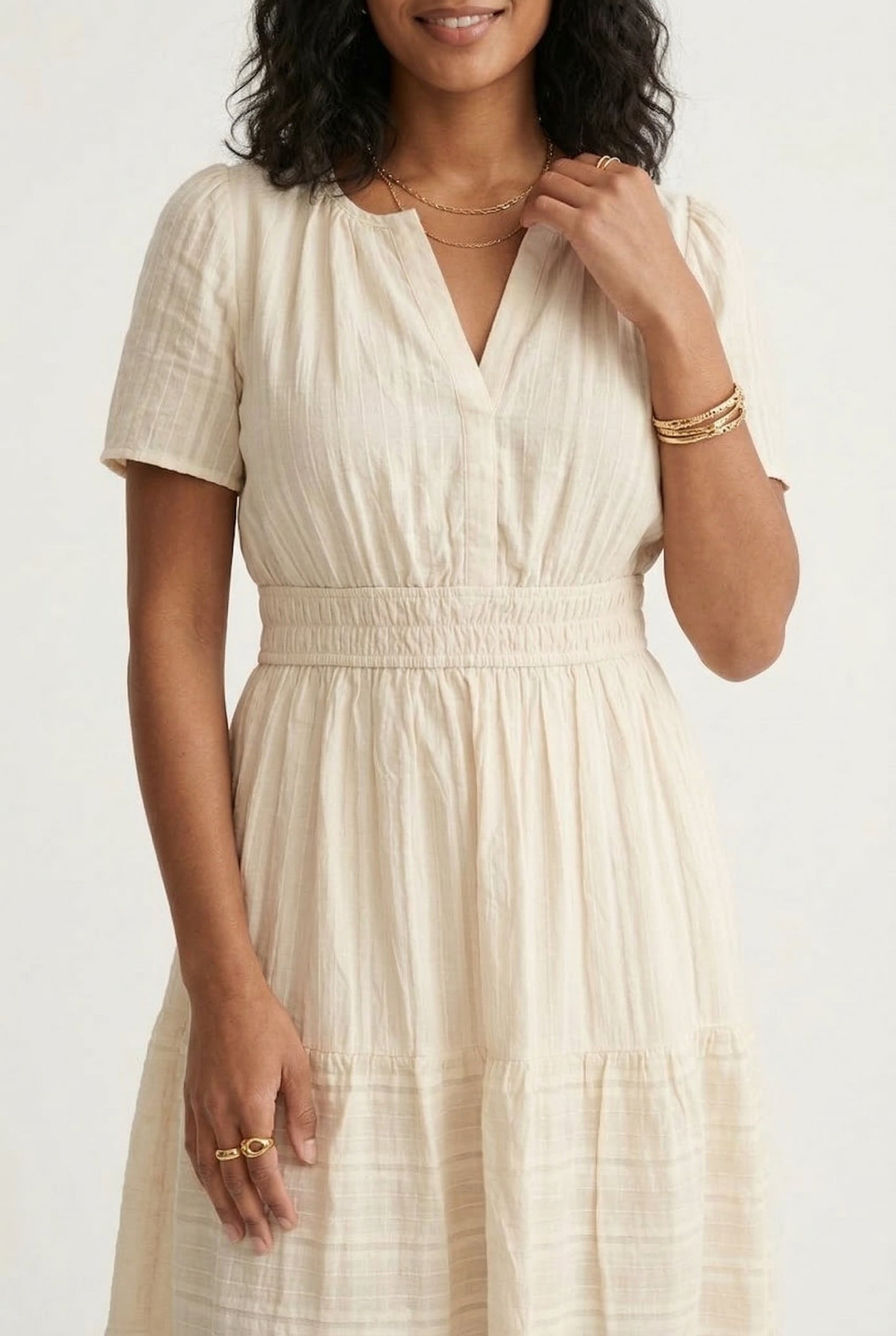 A woman posing in an Oat beige short-sleeve midi dress featuring a button-down bodice and flowy skirt.