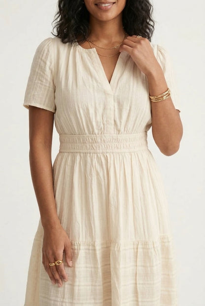 A woman posing in an Oat beige short-sleeve midi dress featuring a button-down bodice and flowy skirt.