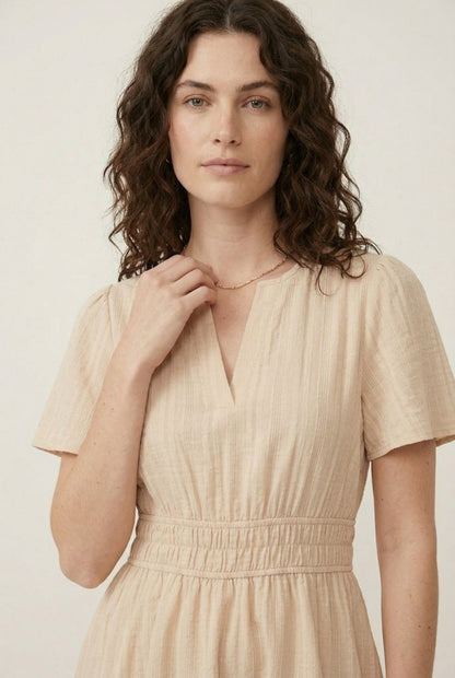 Woman wearing a short sleeve v-neck tiered dress in oat beige color