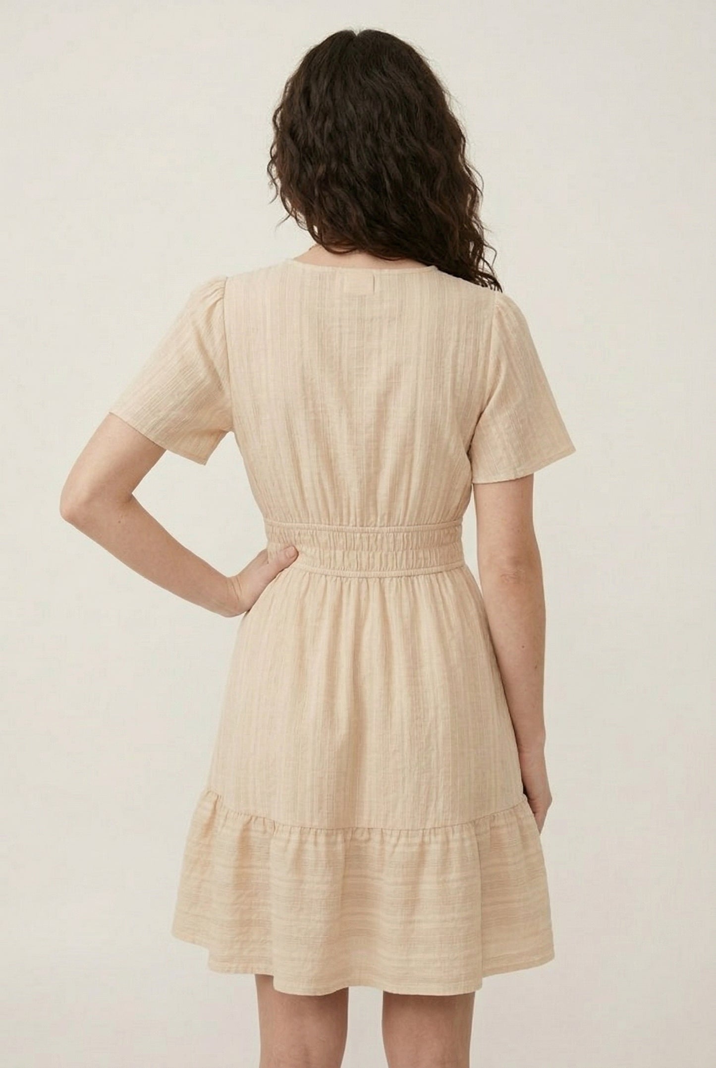 Woman wearing a short sleeve v-neck tiered dress in oat beige color