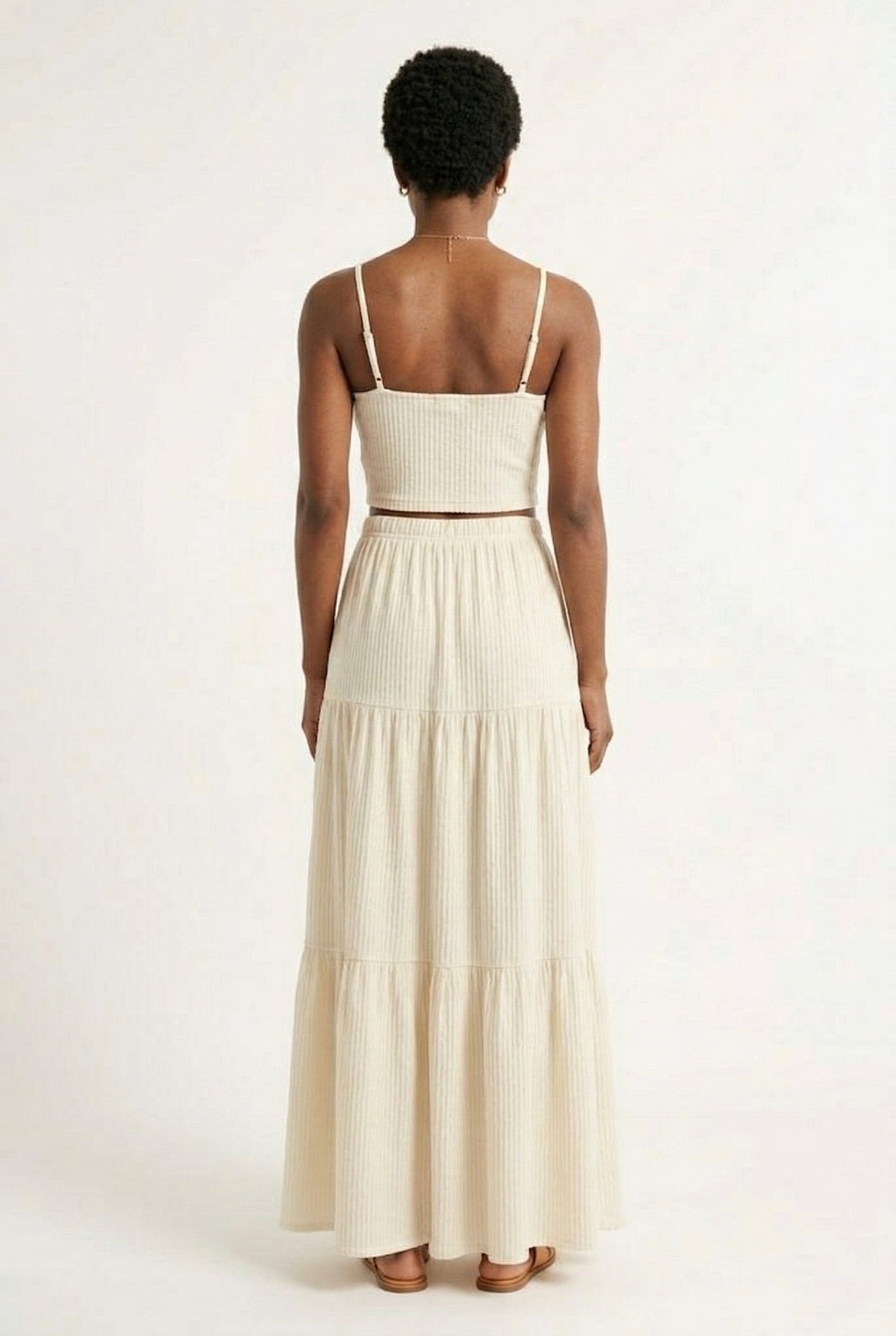 Woman modeling an Oat cream two-piece matching set featuring a spaghetti strap crop top and tiered maxi skirt