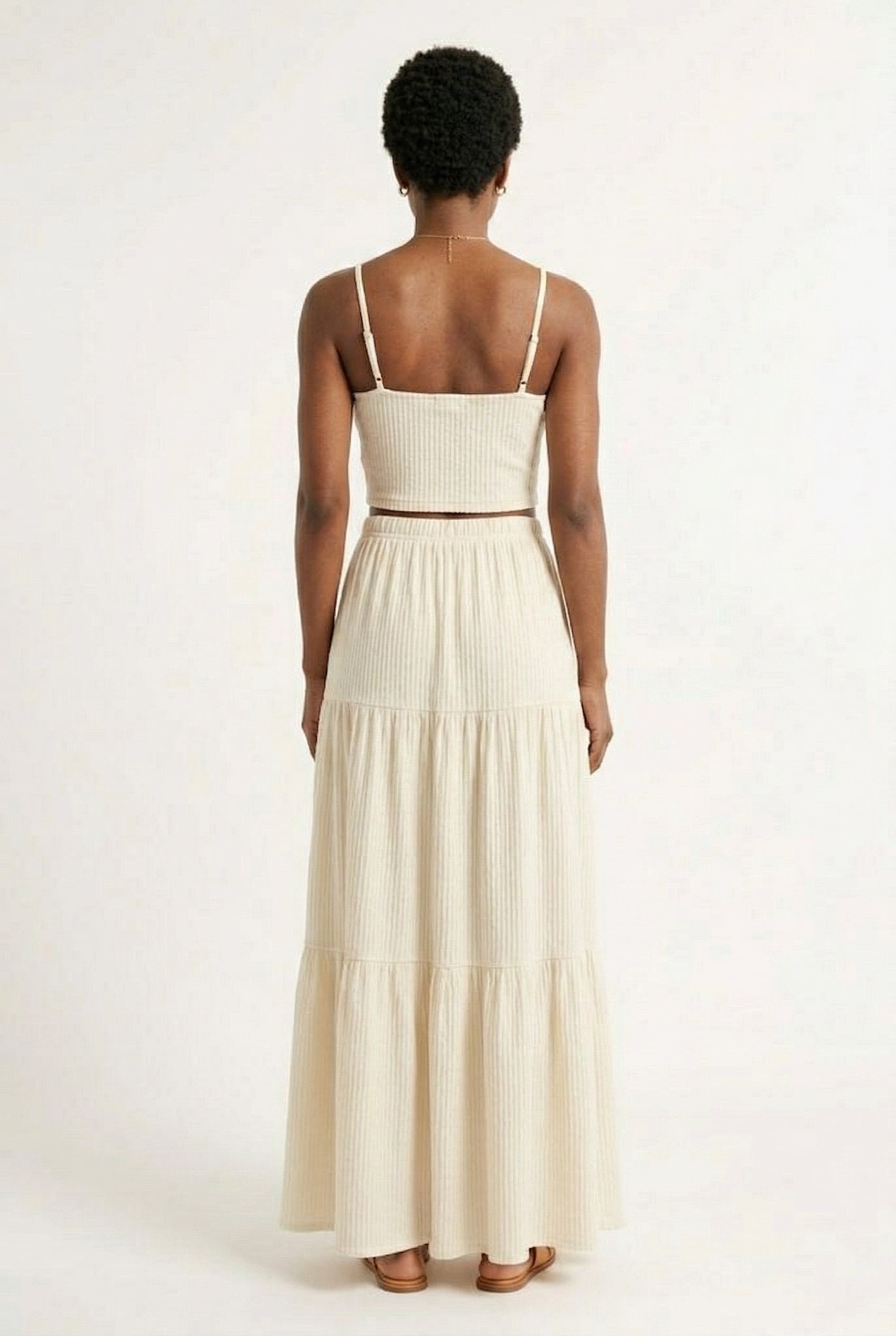 Woman modeling an Oat cream two-piece matching set featuring a spaghetti strap crop top and tiered maxi skirt
