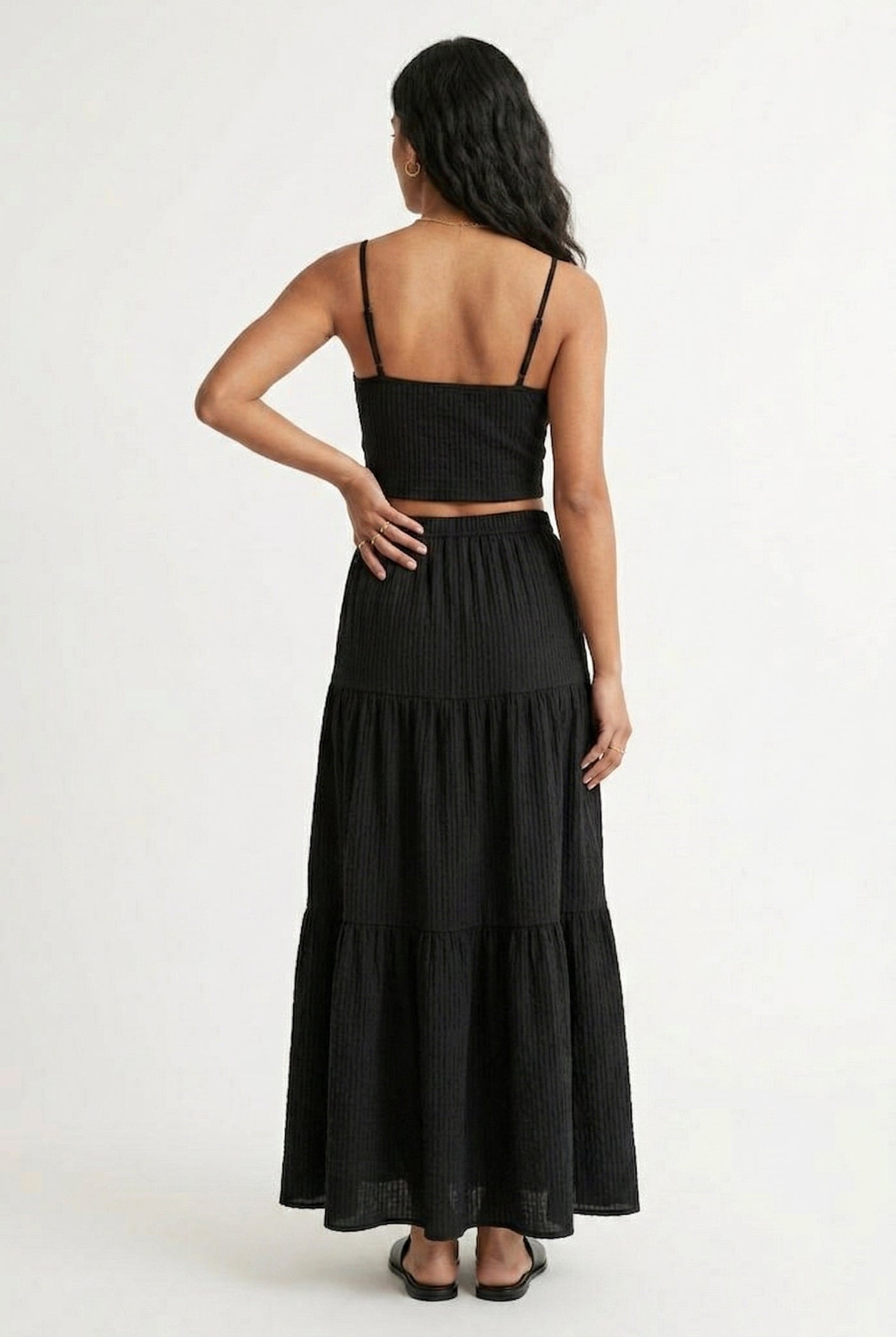 Woman modeling an Obsidian black two-piece matching set featuring a spaghetti strap crop top and tiered maxi skirt