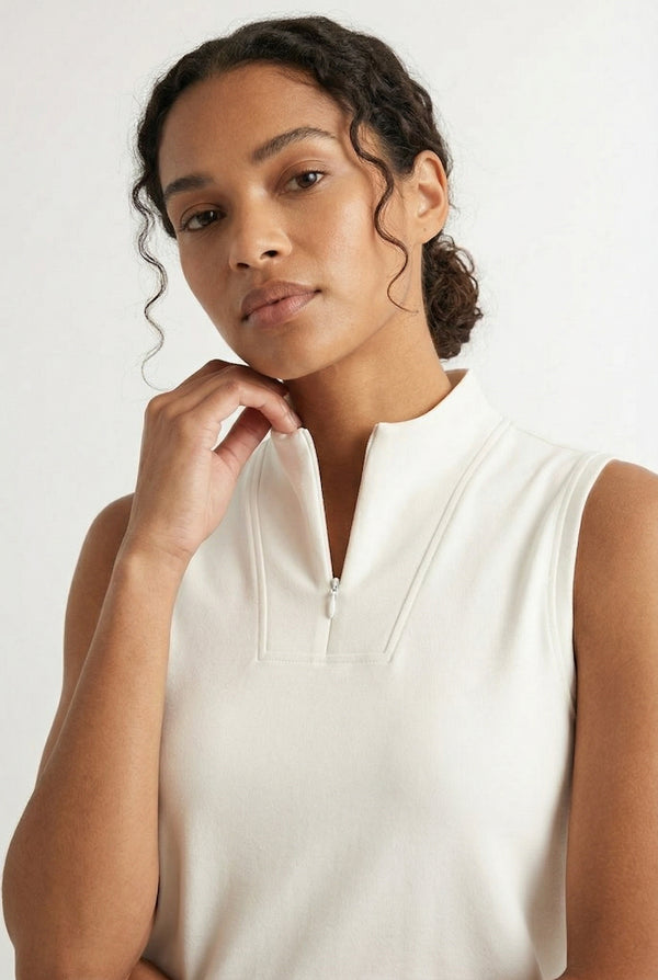 A woman wearing a Birch white sleeveless athletic dress with a high collar and front zipper.