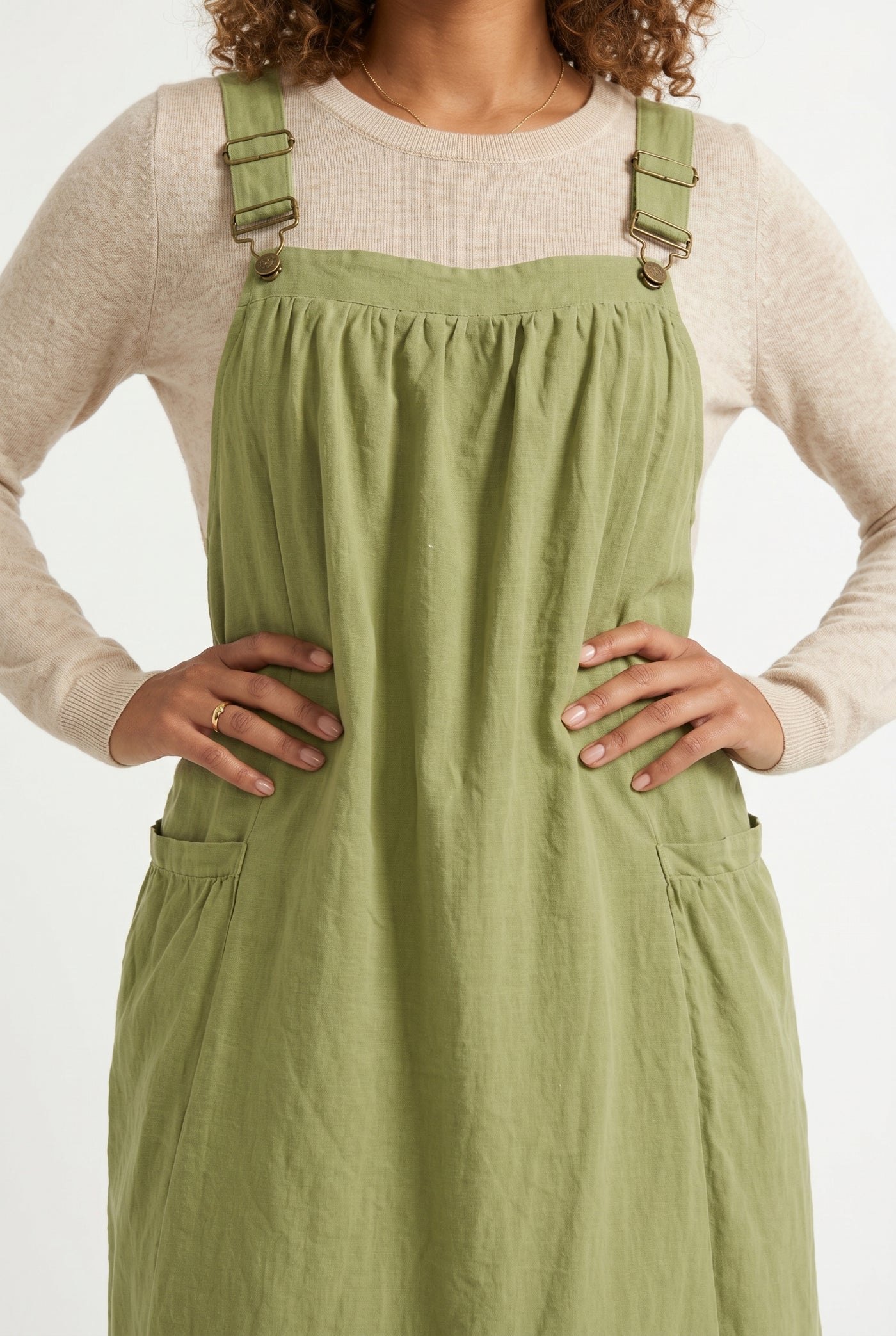 Woman wearing a matcha light green midi-length pinafore dress layered over a white long-sleeve top