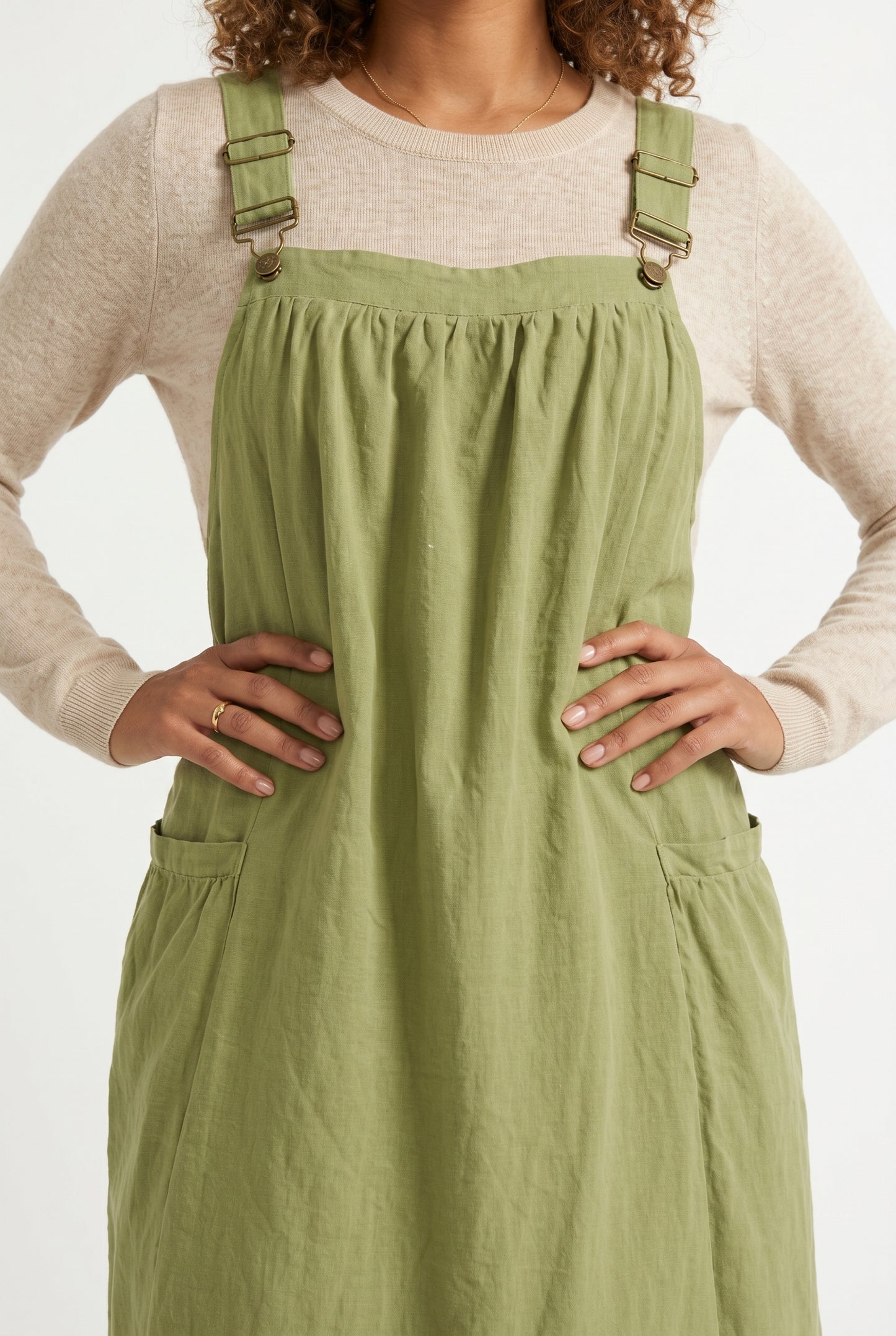 Woman wearing a matcha light green midi-length pinafore dress layered over a white long-sleeve top