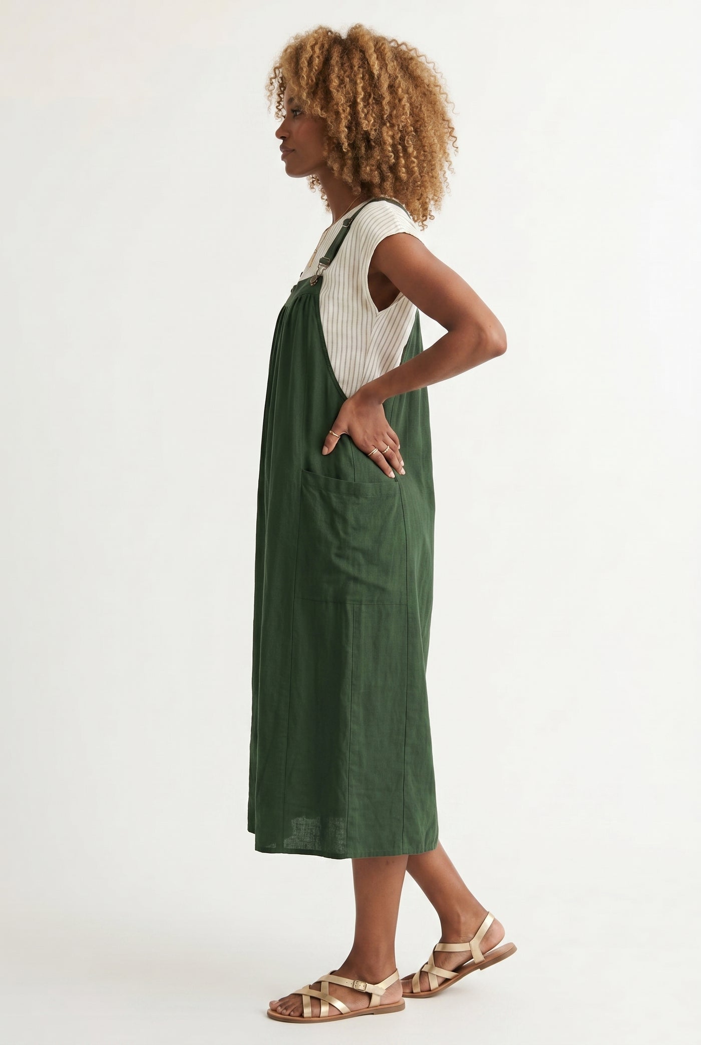 Woman wearing a scarab dark green midi-length pinafore dress layered over a white long-sleeve top