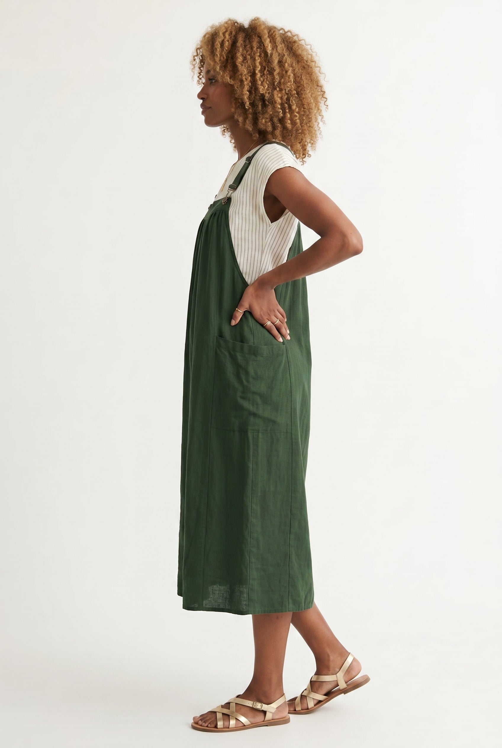 Woman wearing a scarab dark green midi-length pinafore dress layered over a white long-sleeve top