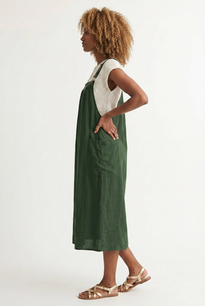 Woman wearing a scarab dark green midi-length pinafore dress layered over a white long-sleeve top