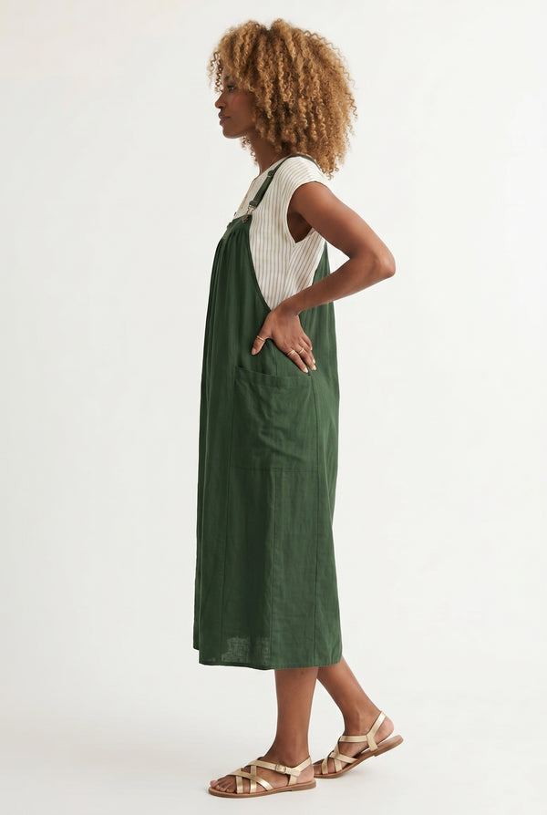 Woman wearing a scarab dark green midi-length pinafore dress layered over a white long-sleeve top