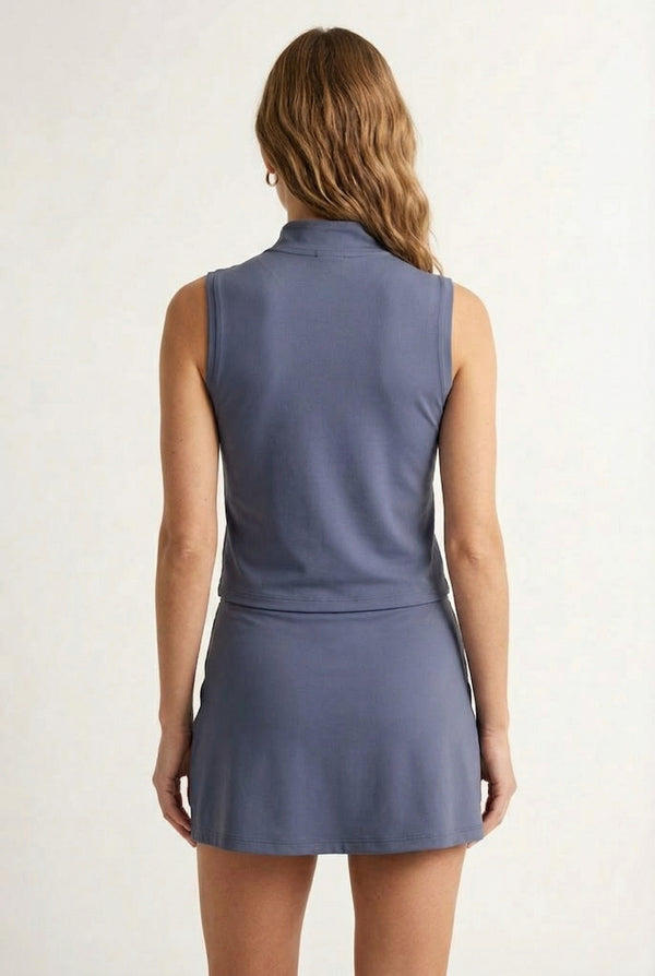A woman modeling a Chambray blue sleeveless athletic dress with a matching skirt and zip-up collar.