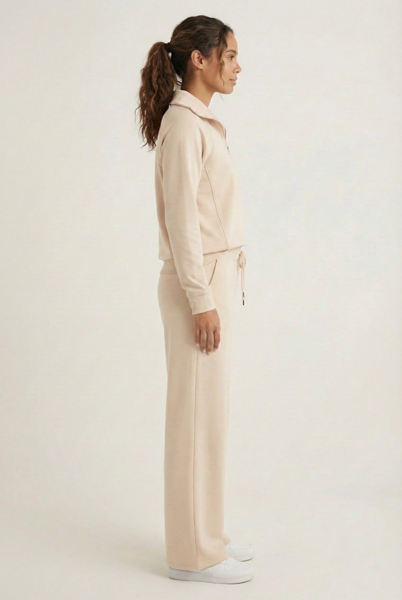 Woman wearing the LOHNR Élan Set in Soft Sand, featuring a smooth, sweatshirt-material half-zip pullover and matching structured pants.