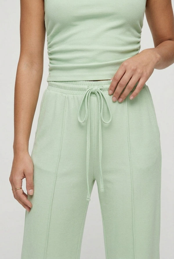 A user interface snippet from an e-commerce platform displaying a product variant row. It shows an unchecked checkbox, a thumbnail image of a model wearing a light green sleeveless jumpsuit, and the text "Sprout" above "5 variants" with a downward-pointing dropdown arrow.
