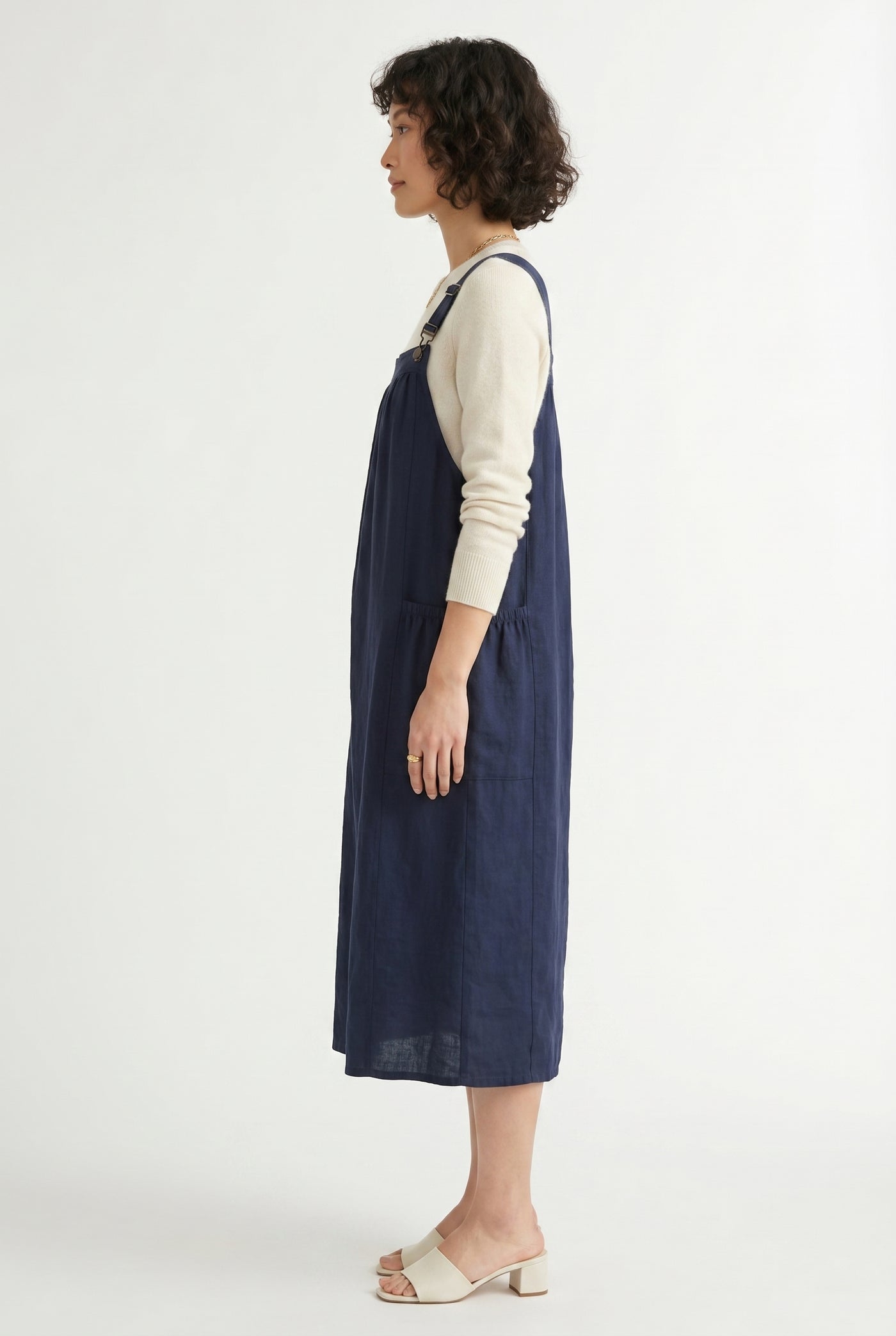 Woman wearing a total eclipse dark navy blue midi-length pinafore dress layered over a white long-sleeve top