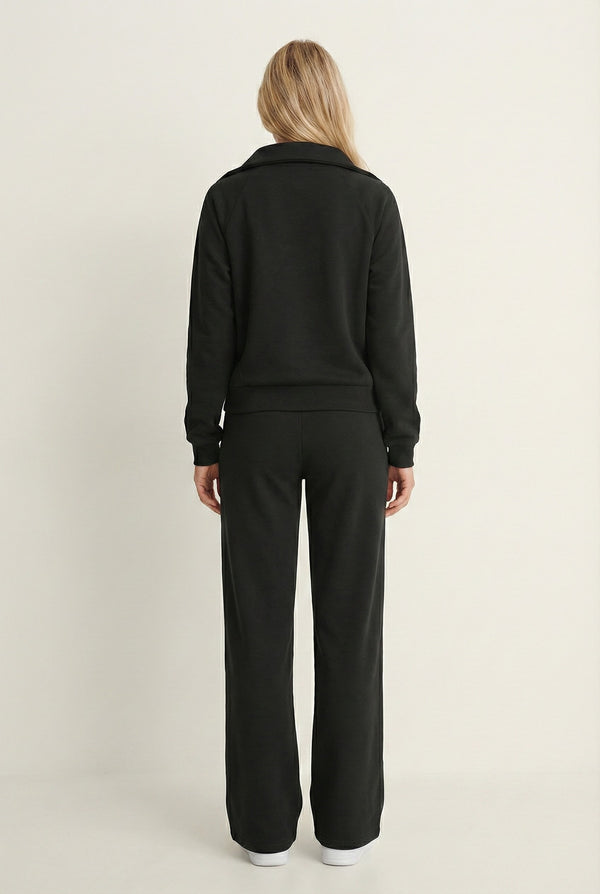 Woman wearing the LOHNR Élan Set in True Black, featuring a smooth, sweatshirt-material half-zip pullover and matching structured pants.
