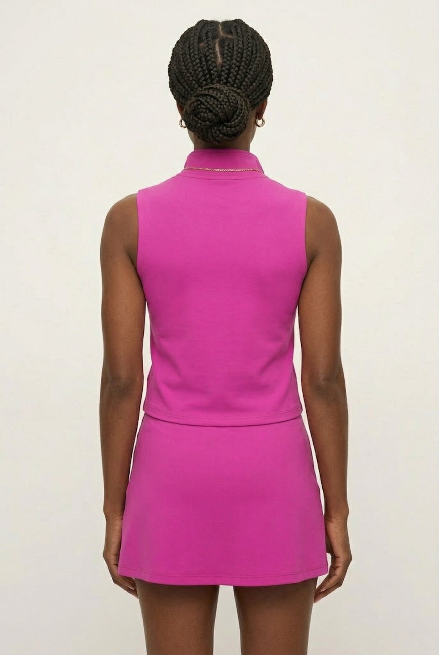 A woman wearing a vibrant Aura Pink sleeveless athletic dress with a zippered high-neck design.