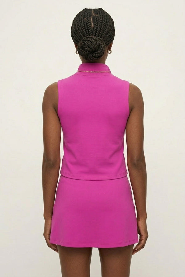 A woman wearing a vibrant Aura Pink sleeveless athletic dress with a zippered high-neck design.