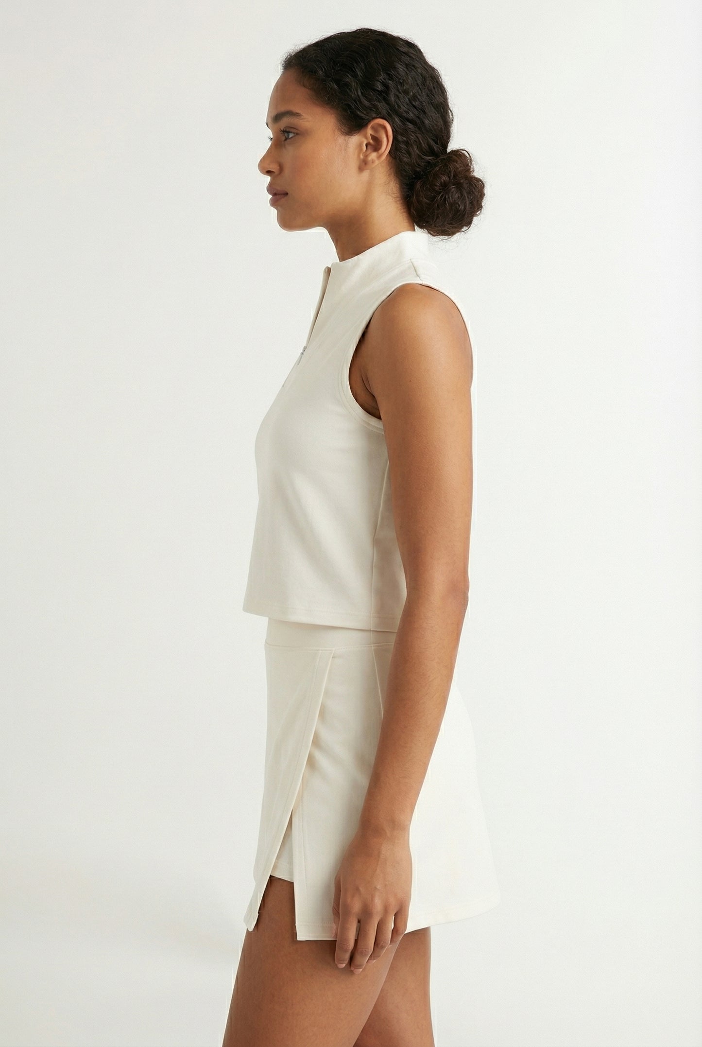 A woman wearing a Birch white sleeveless athletic dress with a high collar and front zipper.