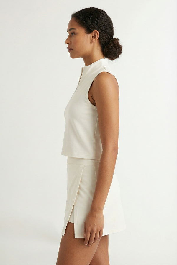 A woman wearing a Birch white sleeveless athletic dress with a high collar and front zipper.