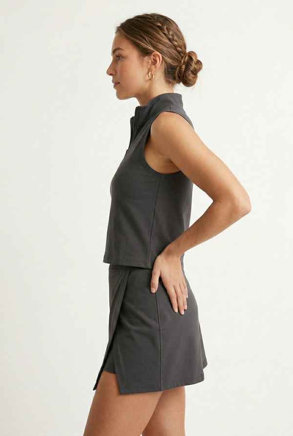 A woman wearing a sleek Black Eyeliner colored sleeveless athletic dress with a mock neck zipper.