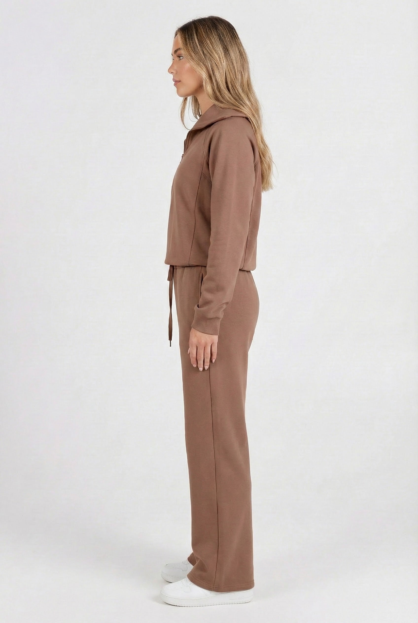 Woman wearing the LOHNR Élan Set in Cocoa Bean, featuring a smooth, sweatshirt-material half-zip pullover and matching structured pants.