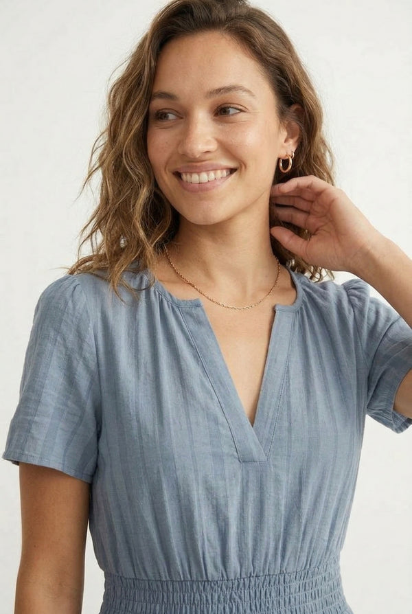 A woman wearing a Cloud Blue short-sleeve midi dress with a button-down front and tiered skirt.