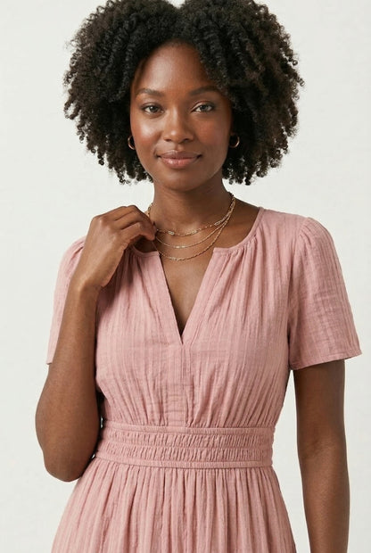 A woman wearing an Antique Pink short-sleeve midi dress with a button-up front and tiered hem.