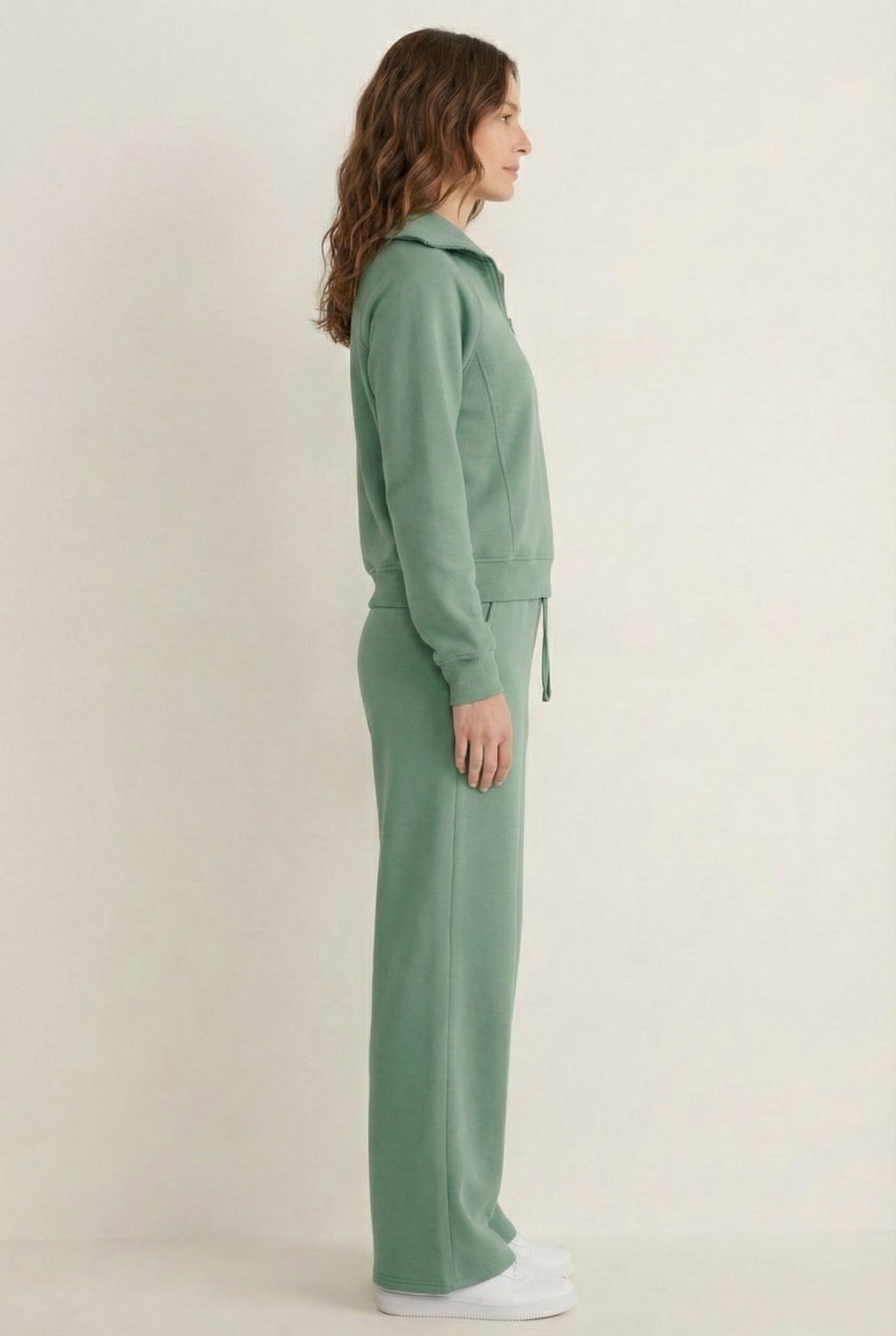 Woman wearing the LOHNR Élan Set in Eucalyptus, featuring a smooth, sweatshirt-material half-zip pullover and matching structured pants.