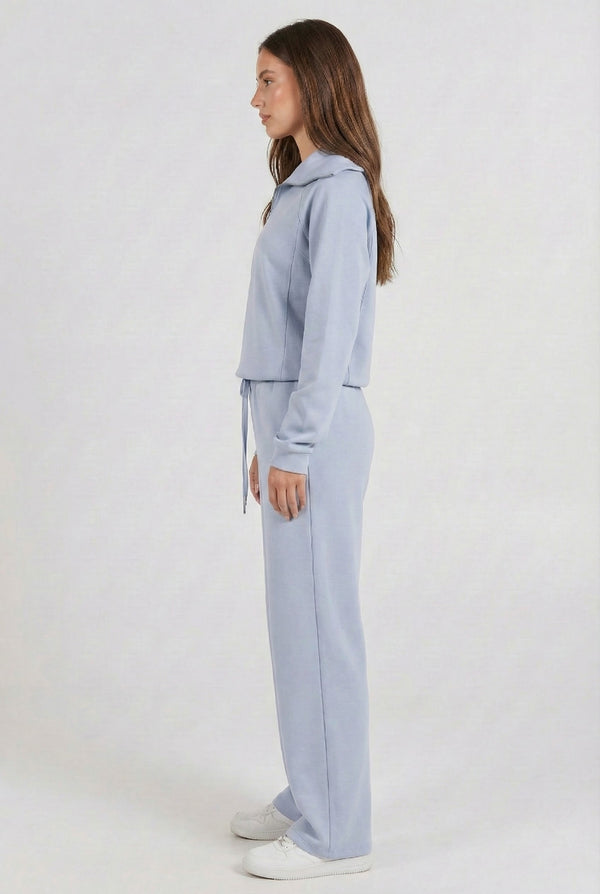 Woman wearing the LOHNR Élan Set in Cloud Blue, featuring a smooth, sweatshirt-material half-zip pullover and matching structured pants.