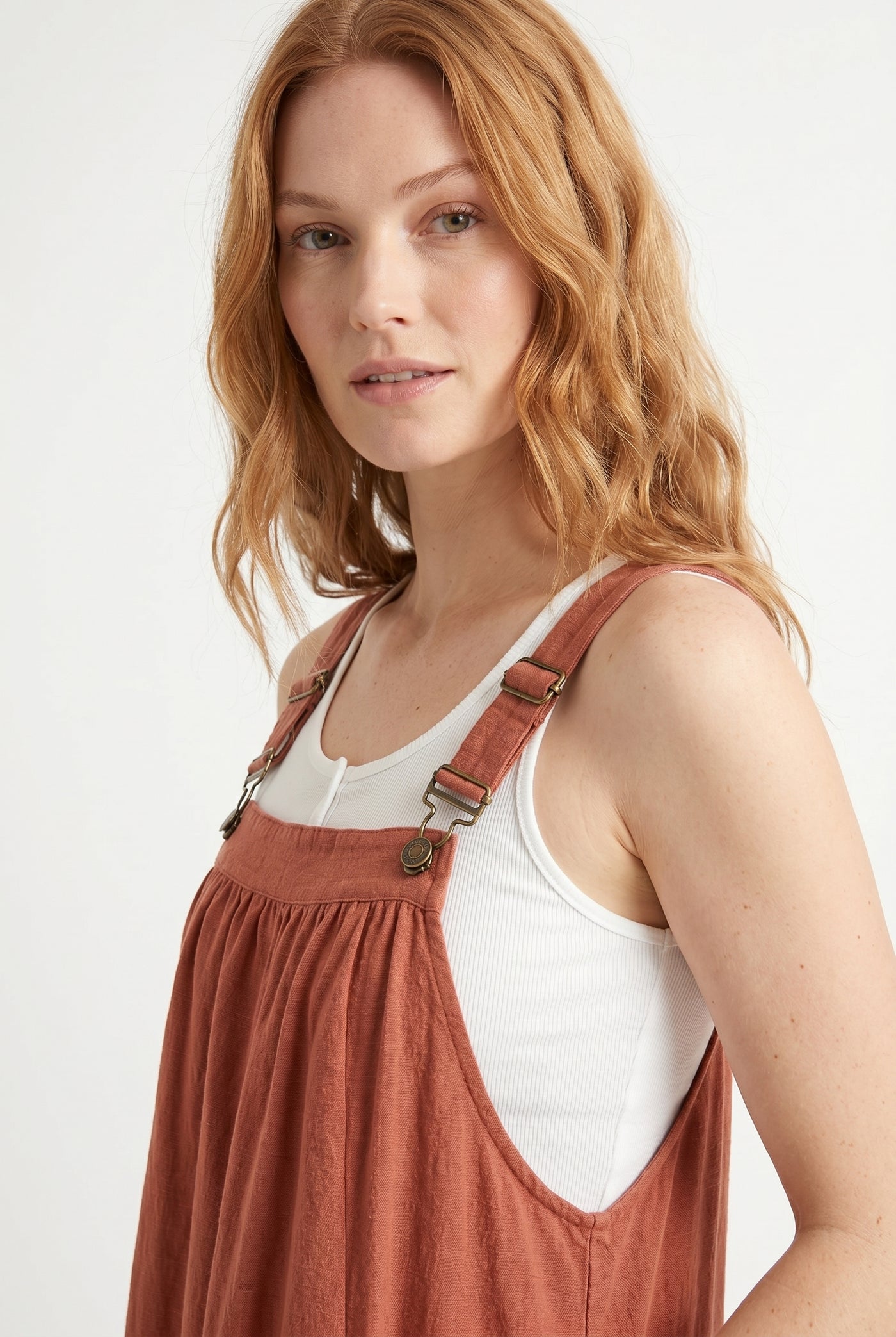 Woman wearing a burnt sienna orange midi-length pinafore dress layered over a white long-sleeve top