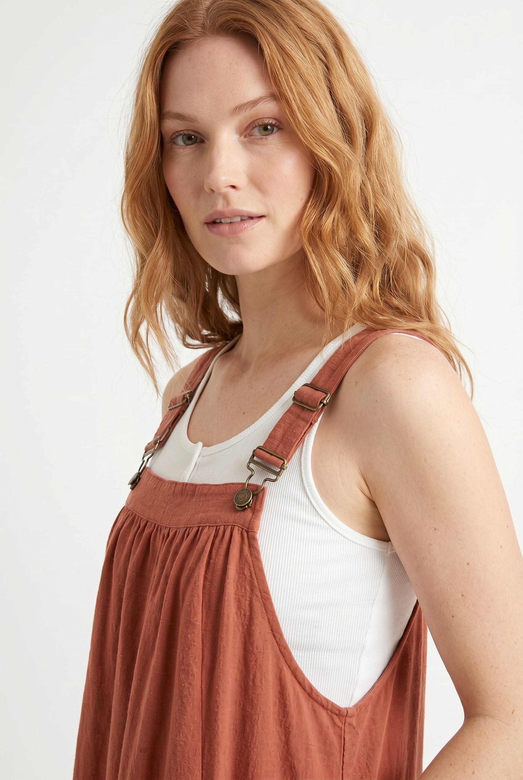 Woman wearing a burnt sienna orange midi-length pinafore dress layered over a white long-sleeve top