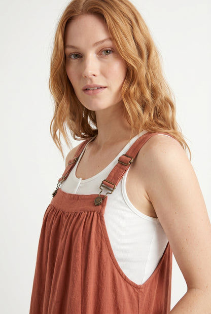 Woman wearing a burnt sienna orange midi-length pinafore dress layered over a white long-sleeve top