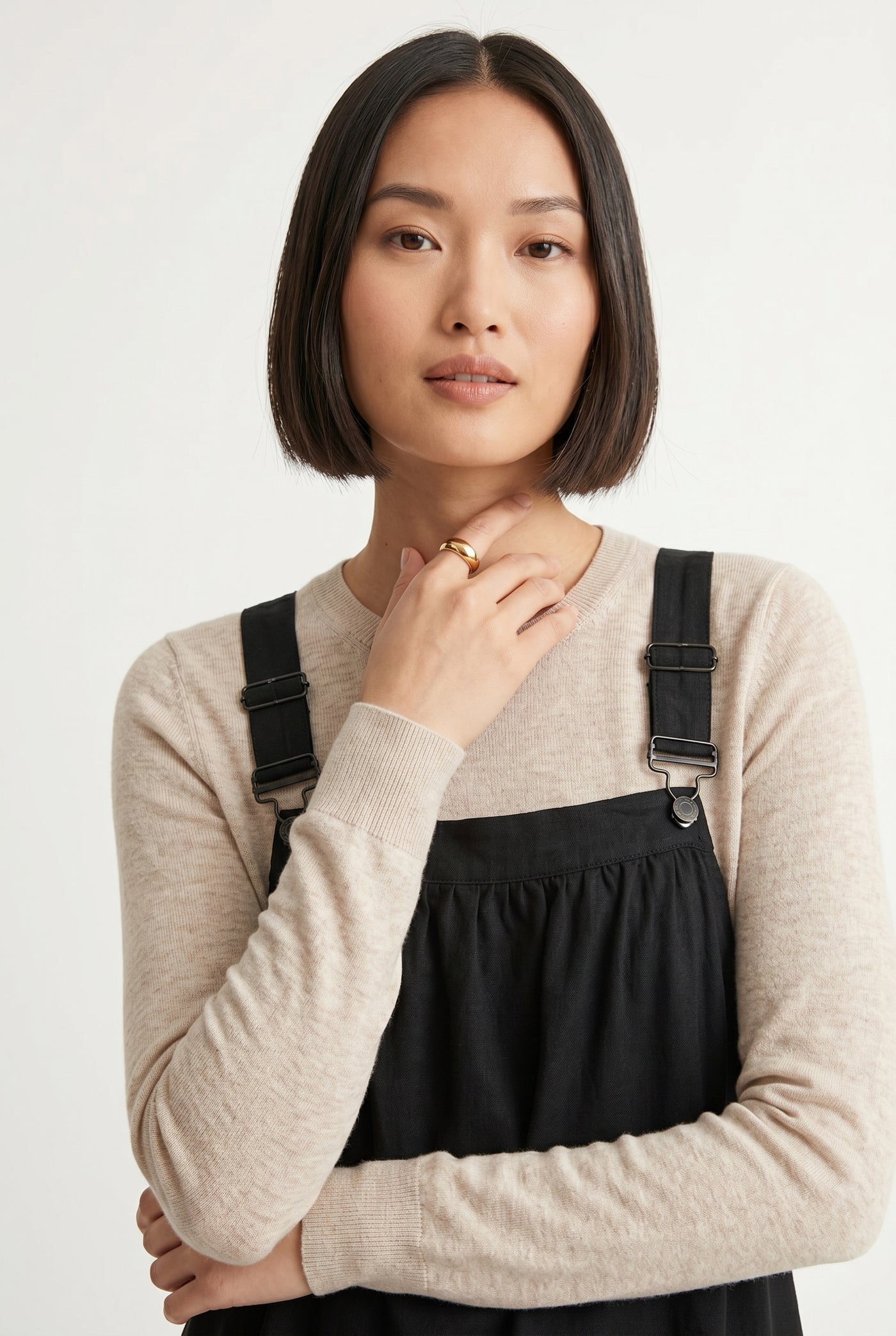 Woman wearing an onyx black midi-length pinafore dress layered over a white long-sleeve top