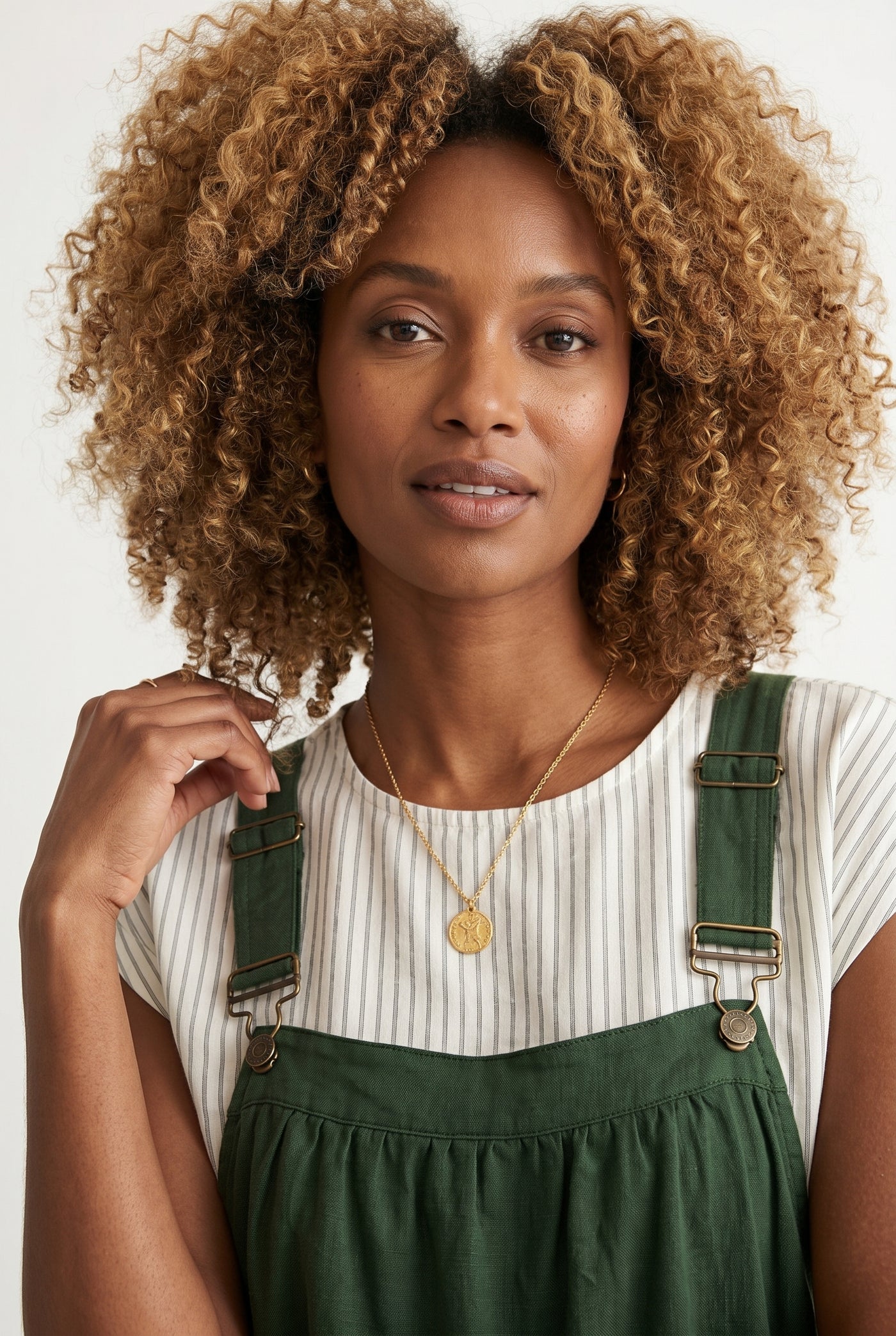 Woman wearing a scarab dark green midi-length pinafore dress layered over a white long-sleeve top