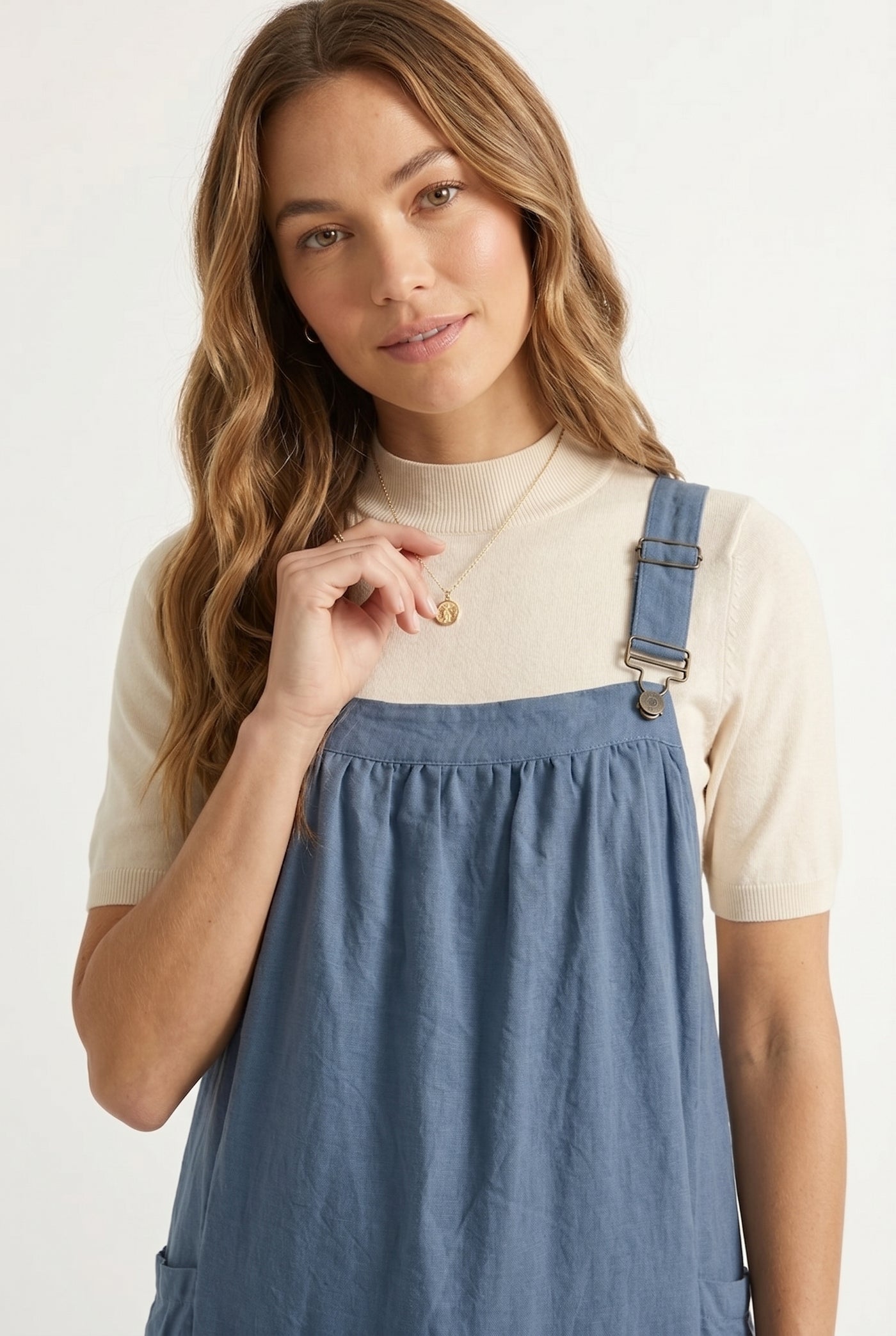 Woman wearing a storm blue midi-length pinafore dress layered over a white long-sleeve top