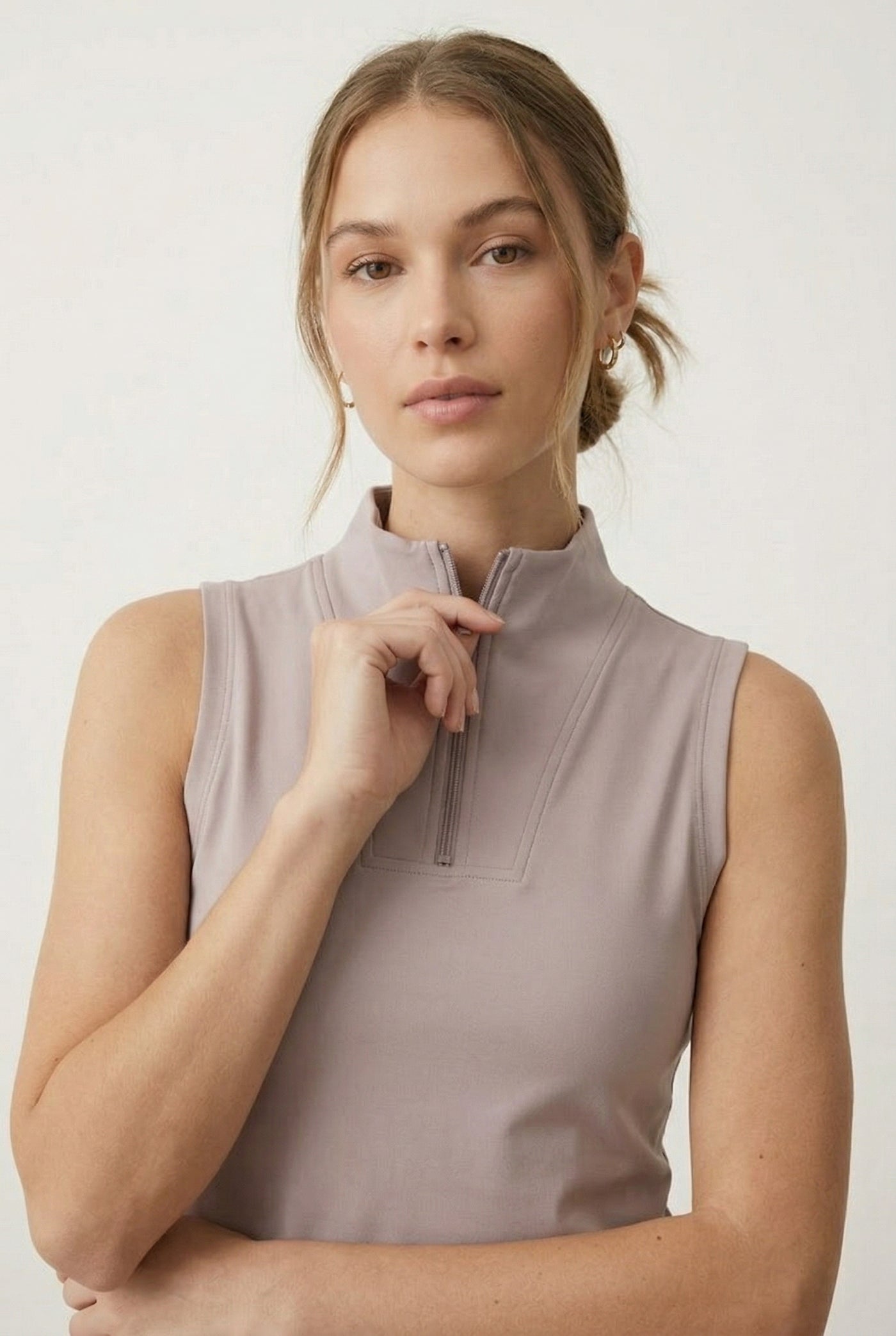 A woman posing in a Stone Veil colored sleeveless sporty dress featuring a zip-up mock neck.